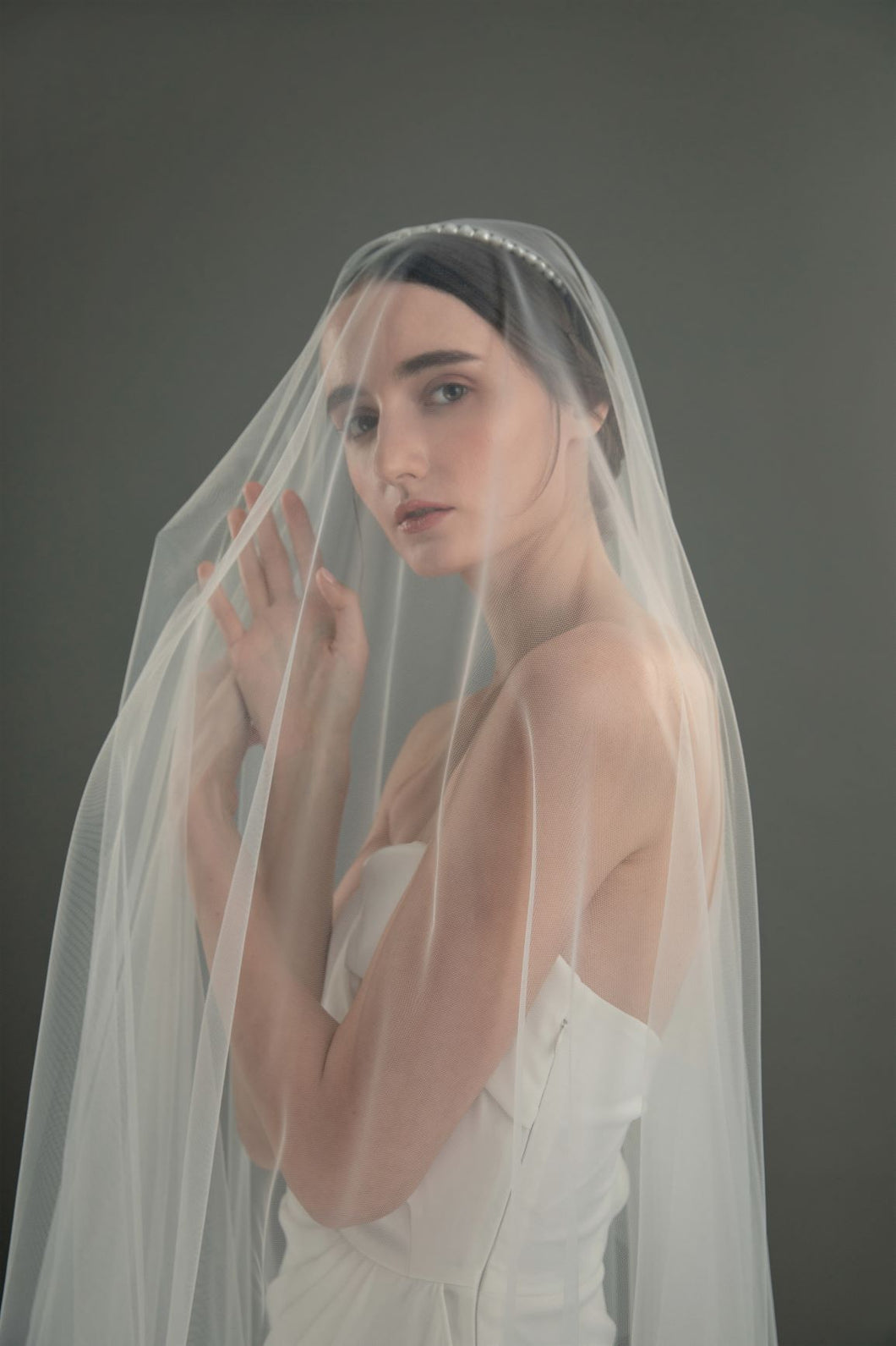 Model in white wedding dress wearing modern lux hair jewelry GALIA Single Row Baroque Pearl Headband, covered in veil